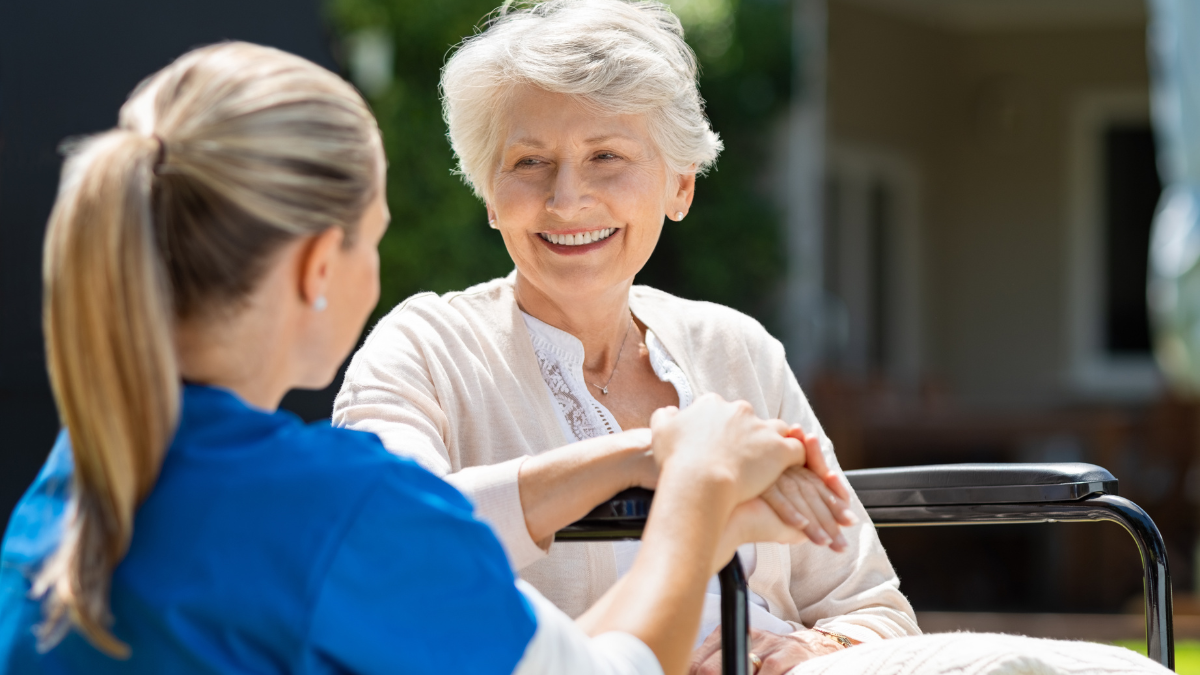 elderly patient sat smiling whilst medical professional holds their hand