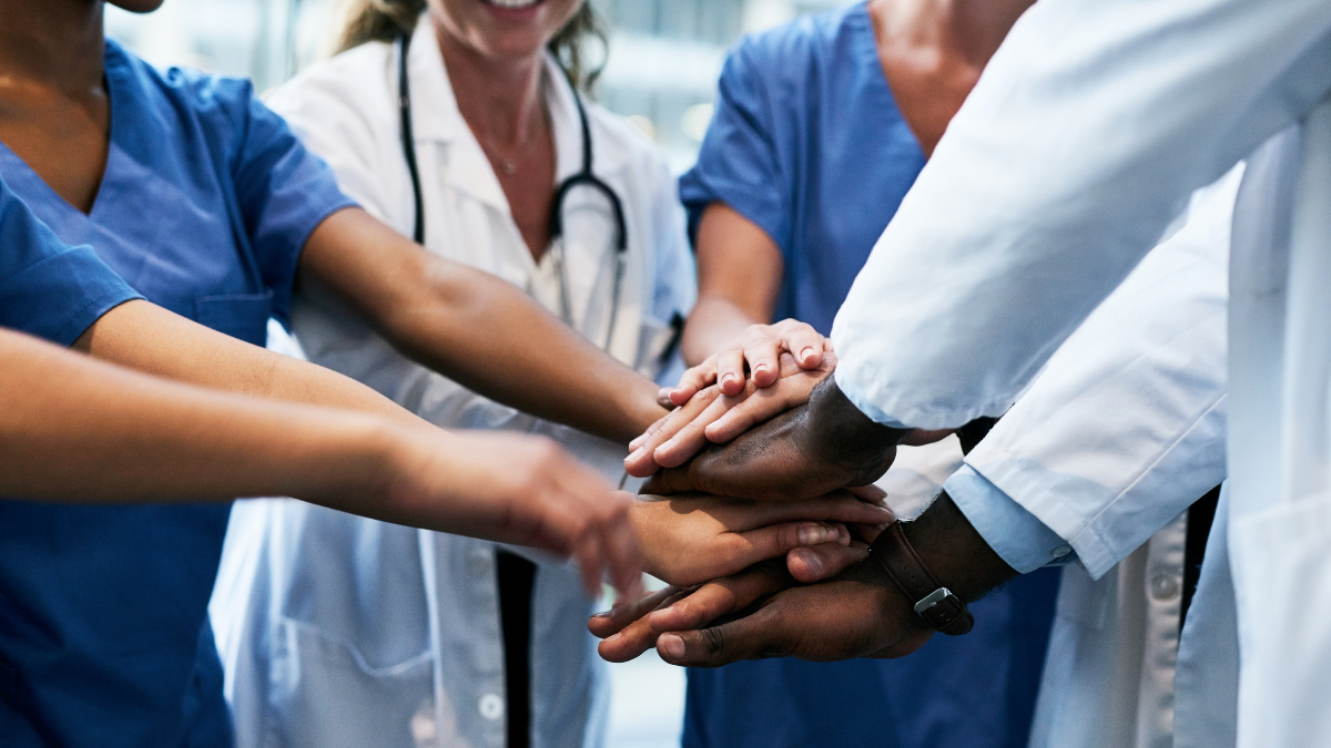 medical professionals holding hands together in the middle of a huddle