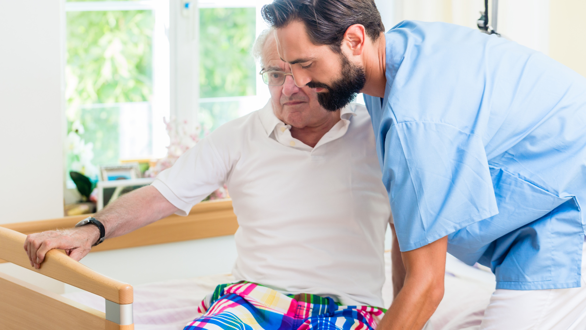 Healthcare professional helping male patient off the bed