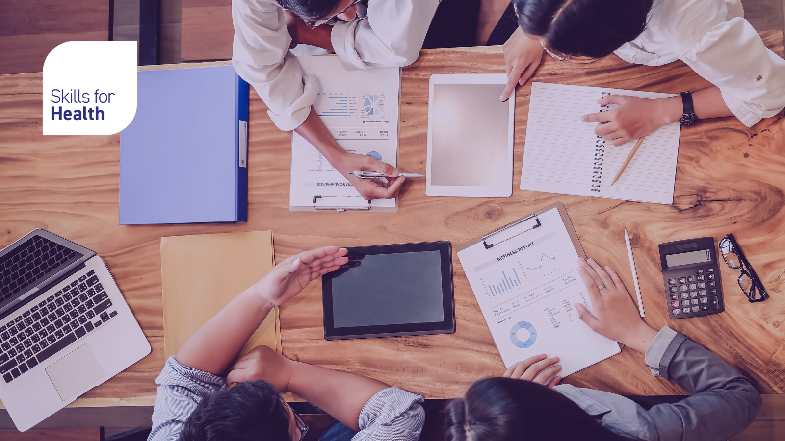 four professionals sat around a table inspecting and reviewing paper documents with some laptops and binders