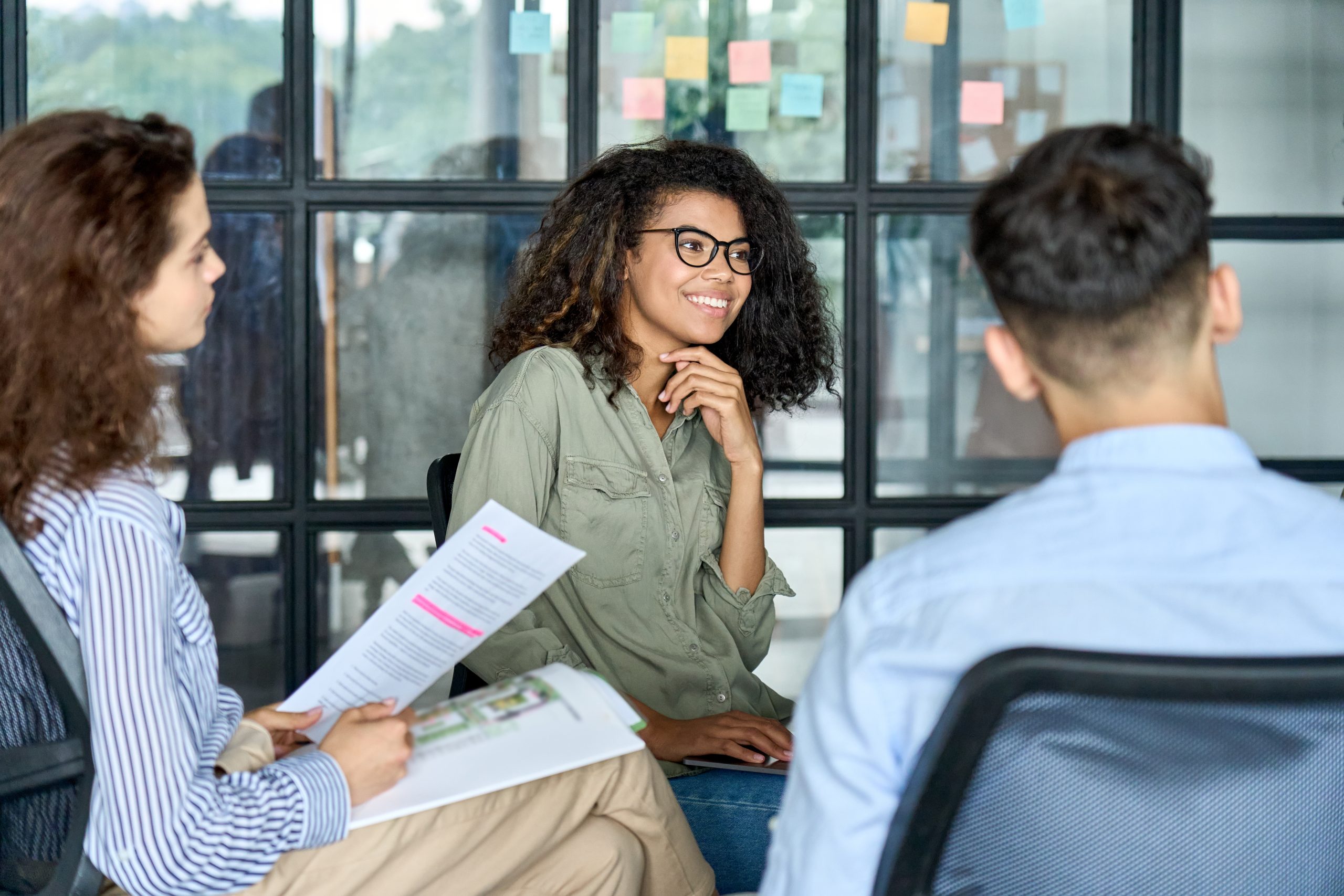 group of people sat around a circle at what appears to be a work meeting, one is holding a piece of paper with highlighted text on it