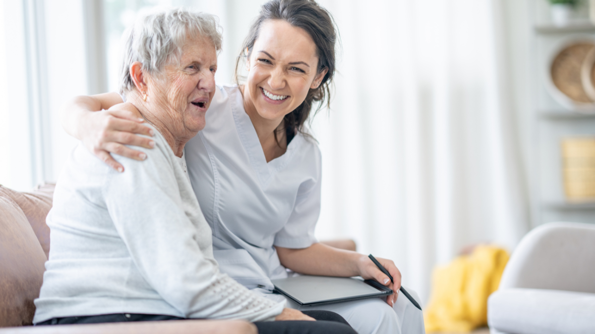 elderly patient with medical professional sat on a sofa, they're smiling together