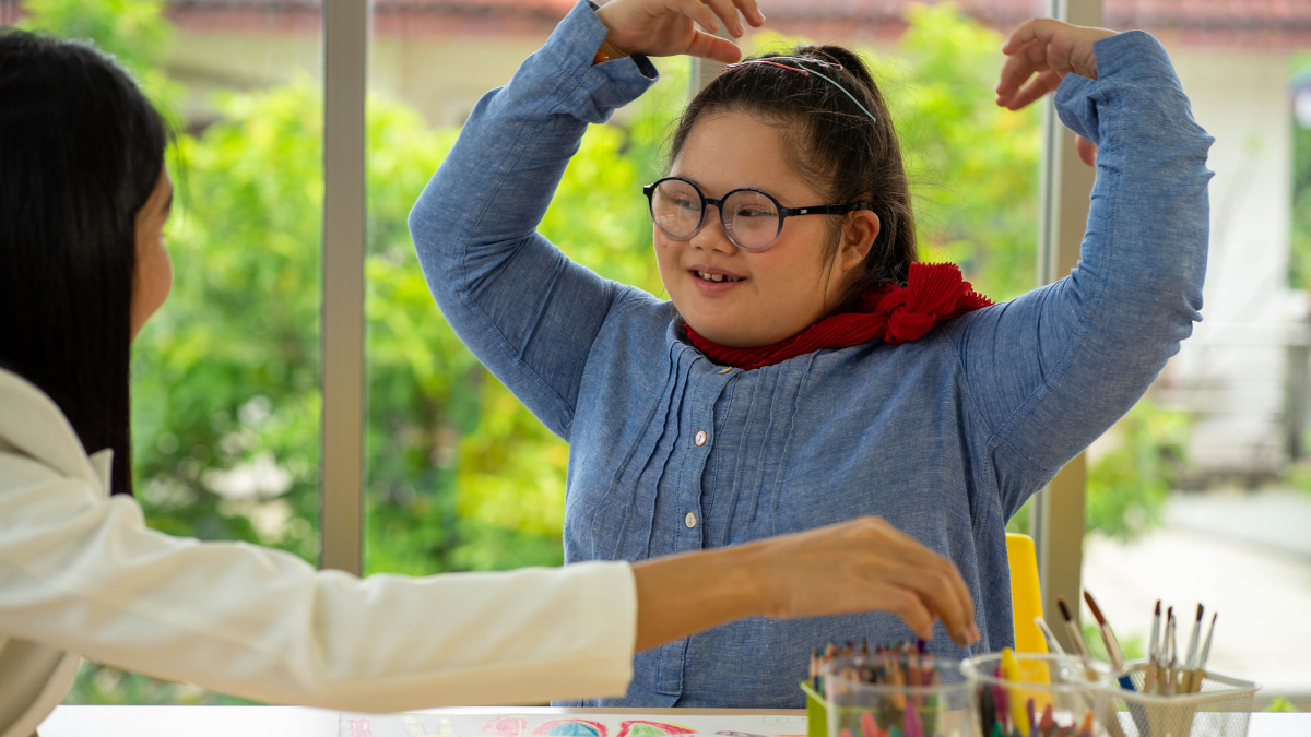 Professional assisting a child with disabilities at a school desk