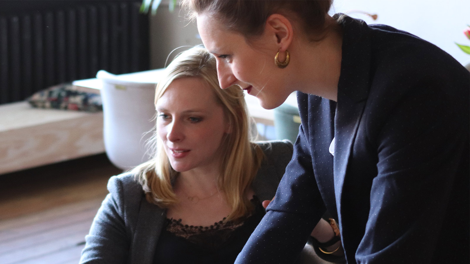two women, one sat, one stood over, helping