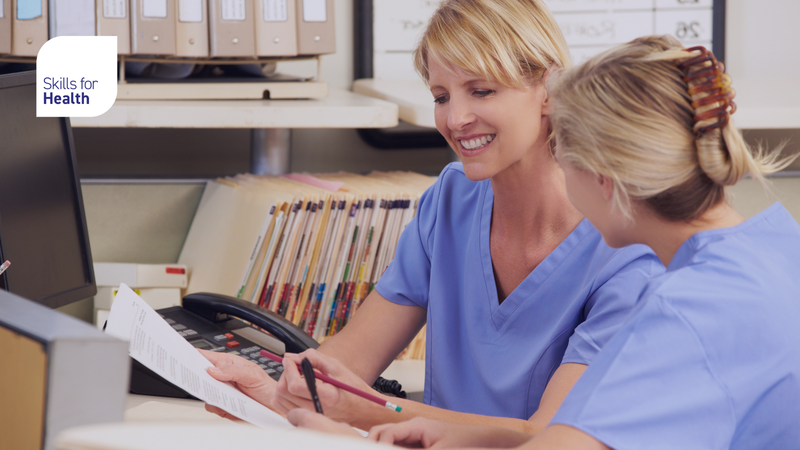 two medical works sat looking at sheet of paper smiling