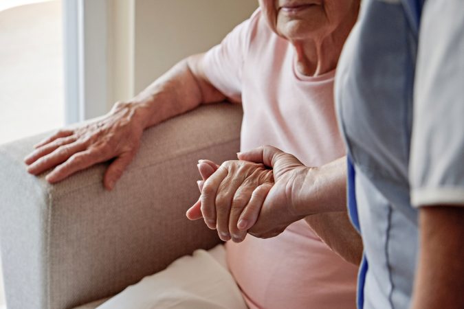 Mature female in elderly care facility gets help from hospital personnel nurse.