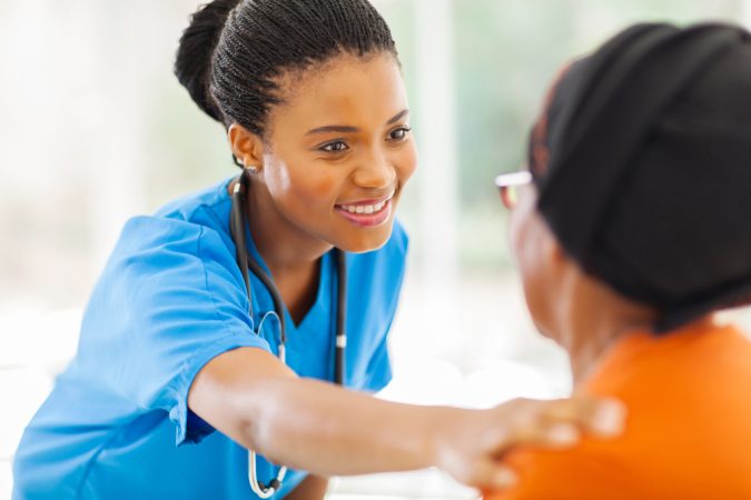 A person in scrubs smiles while placing a hand on another person's shoulder.