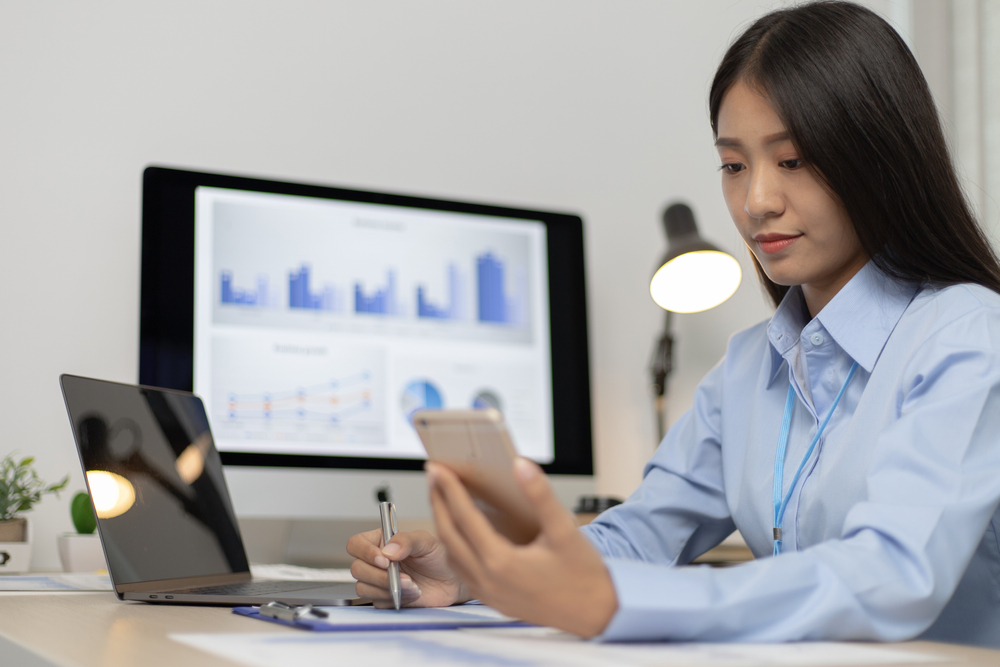 Asian female employees are analyzing market data via smartphones and have laptops to calculate the company's finances In a private office at home, Working at home and new normal concept.