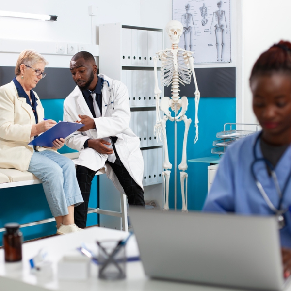 . Physician wearing lab coat is consulting with elderly female patient in clinic office.