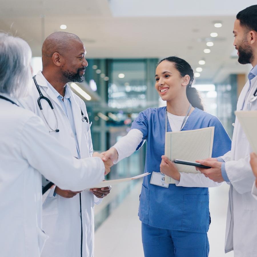 Group of uniformed people in healthcare setting looking happy, two people shake hands