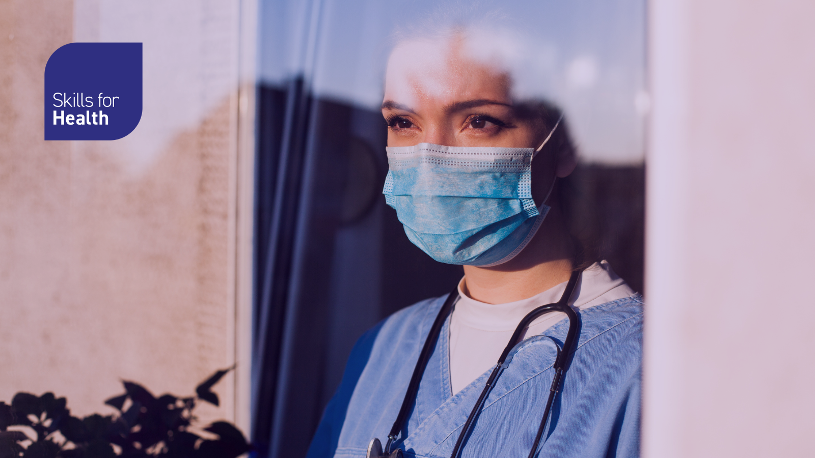 Picture of female medical worker wearing scrubs and face mask looking out the window.
