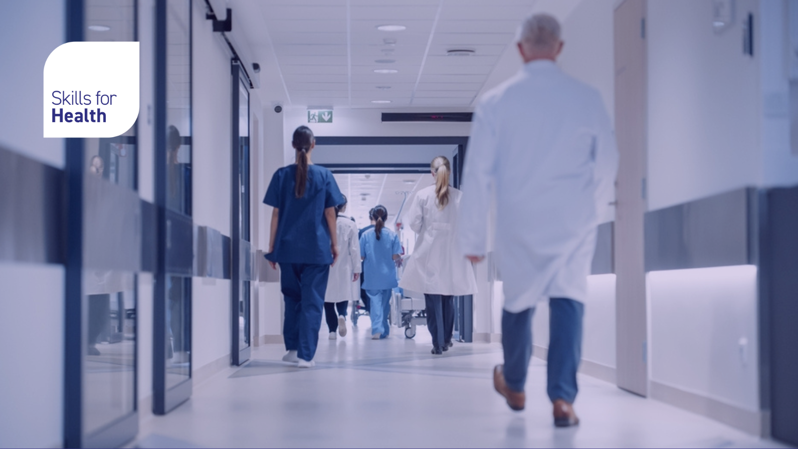 Hospital Hallway with Doctors, Nurses and Specialists in Hospital. Female and Male Physicians, Surgeons, Healthcare Officials Walk Together in Corridor with Their Back to Camera