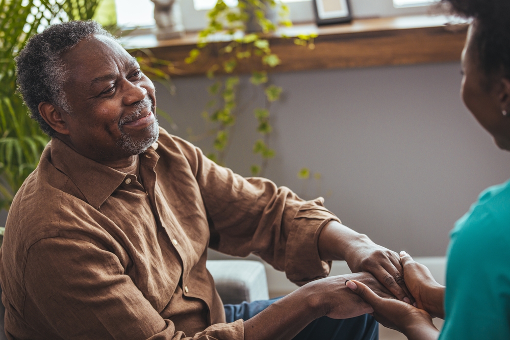 Female healthcare worker holding hands of senior man at care home, focus on hands. Doctor helping old patient with Alzheimer's disease. Female carer holding hands of senior man