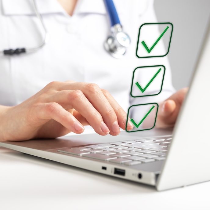 Doctor working on laptop and taking survey, ticking answers at screen. Woman in lab coat sitting at table with computer. Health care, medicine concept.